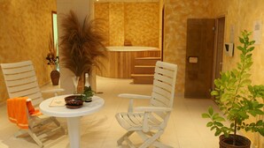 Un hall d’hôtel avec une table ronde, deux chaises blanches, un banc en bois, une plante en pot et une porte en bois.