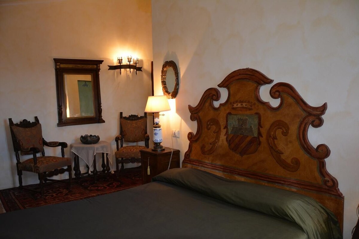 A room with a wooden bed, a chair, a small table, a lamp, and a mirror on the wall.