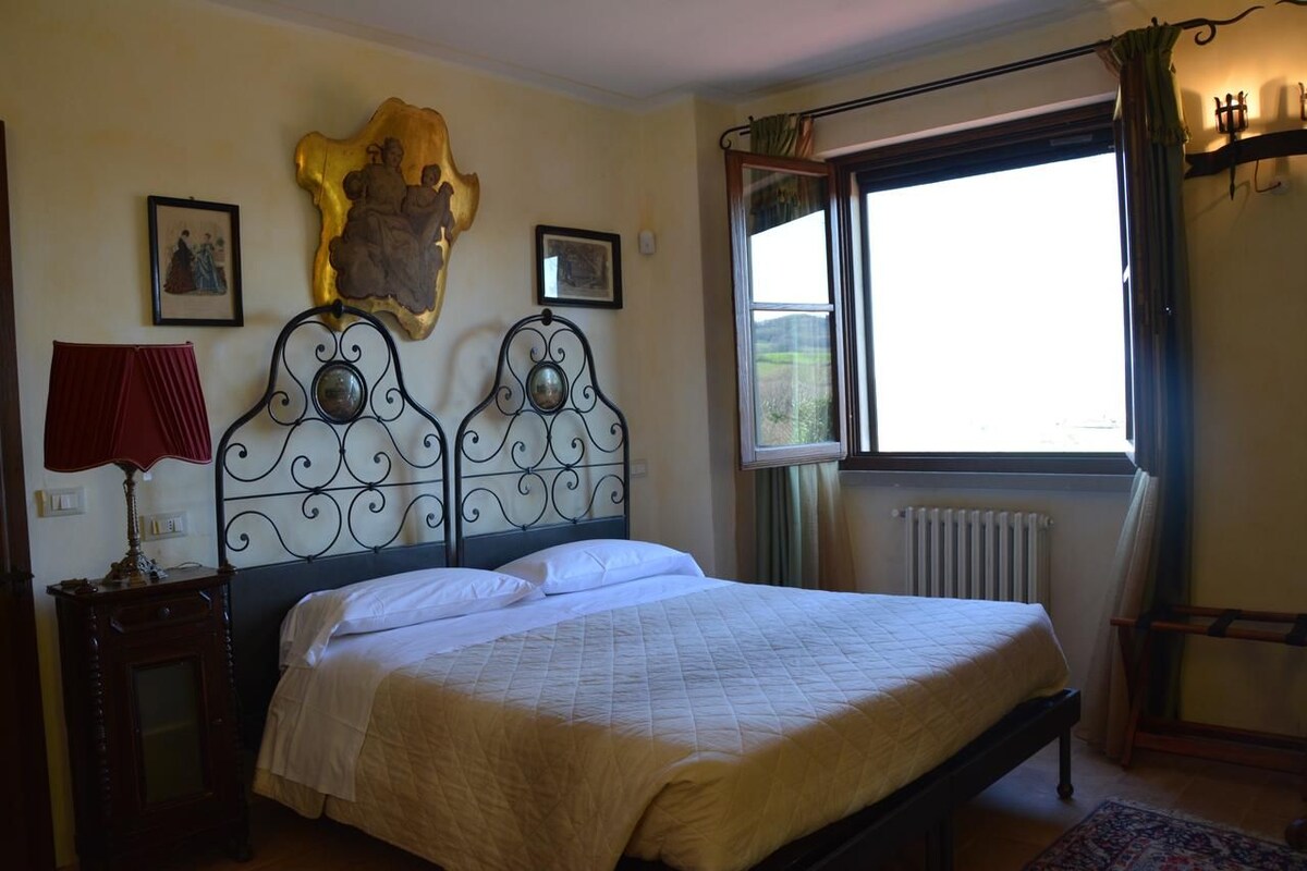 Un dormitorio con cama, ventana con cortinas, radiador y una obra de arte en la pared.