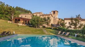 A pool with lounge chairs, a stone building with a tower, and a grassy area.