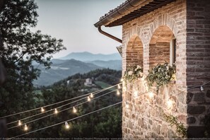 A stone building with arched windows and a string of lights. - Abbazia San Faustino Residenza d'Epoca (Pietralunga)