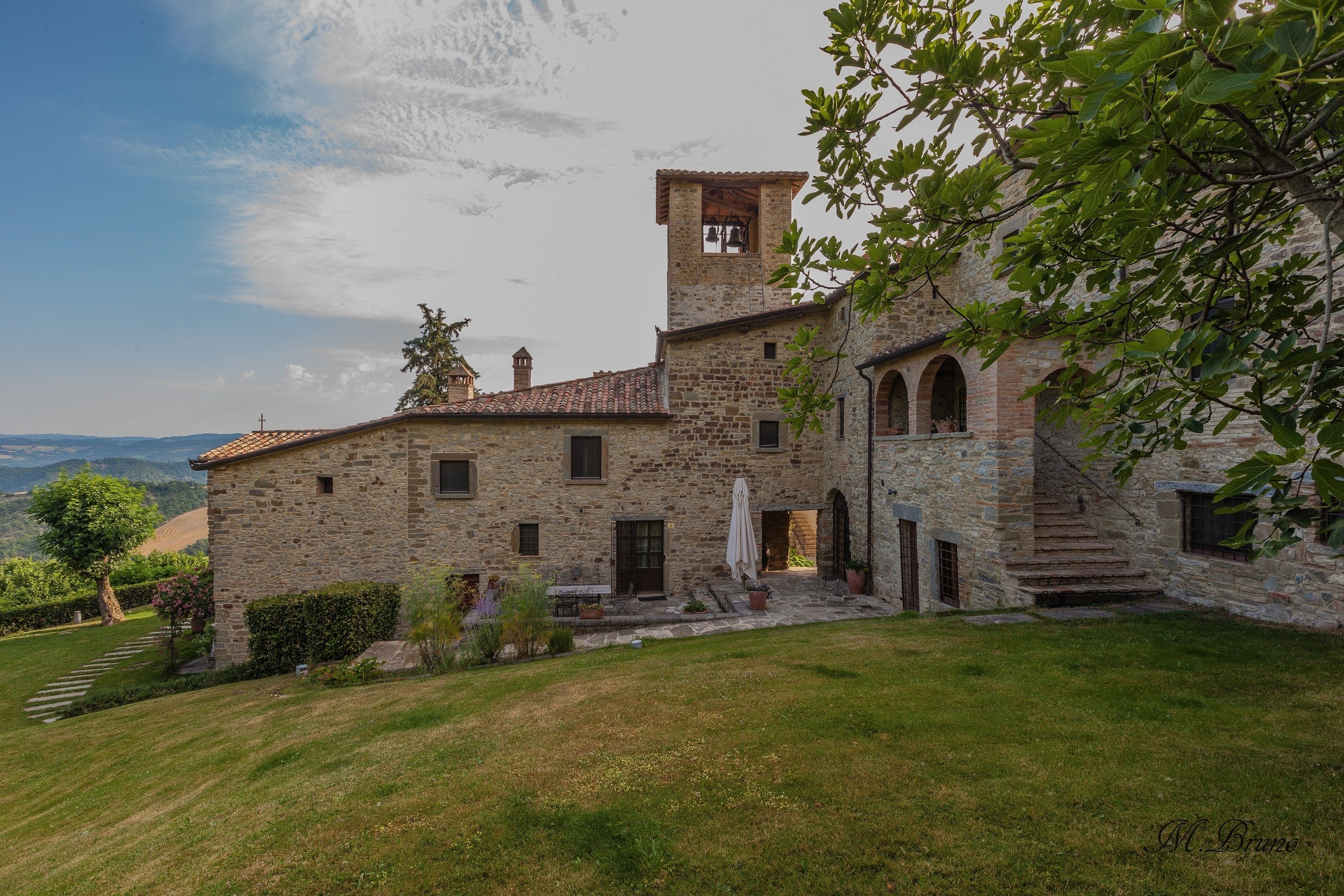 A stone building with a bell tower, a staircase, and a grassy courtyard.
