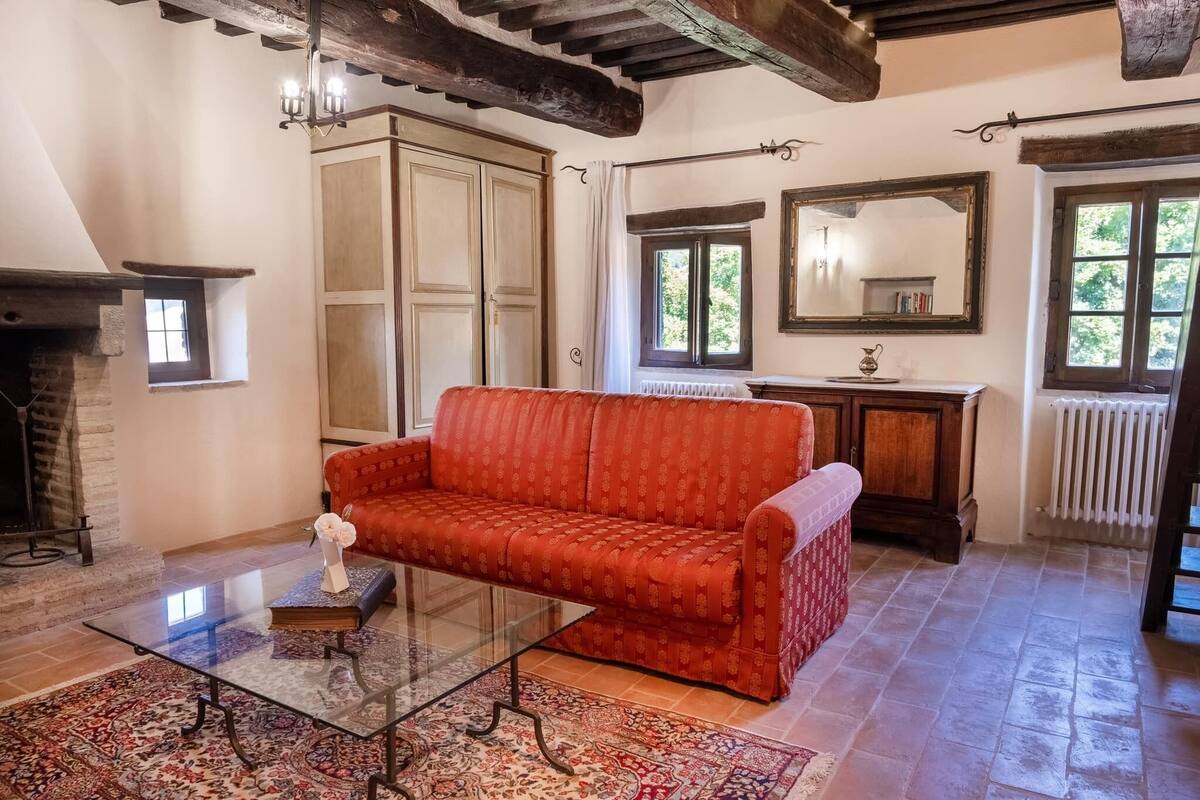 Una habitación acogedora con un sofá rojo, una mesita de cristal, una chimenea y un espejo grande.