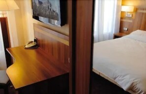 A hotel room with a bed, a desk with a telephone, and a television mounted on the wall.