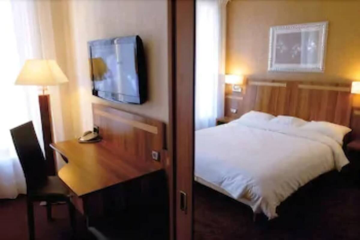 A hotel room with a bed, a desk with a telephone, a television, and a framed picture on the wall.