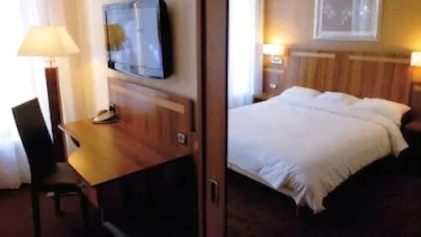 A hotel room with a bed, a desk with a telephone, a television, and a framed picture on the wall.