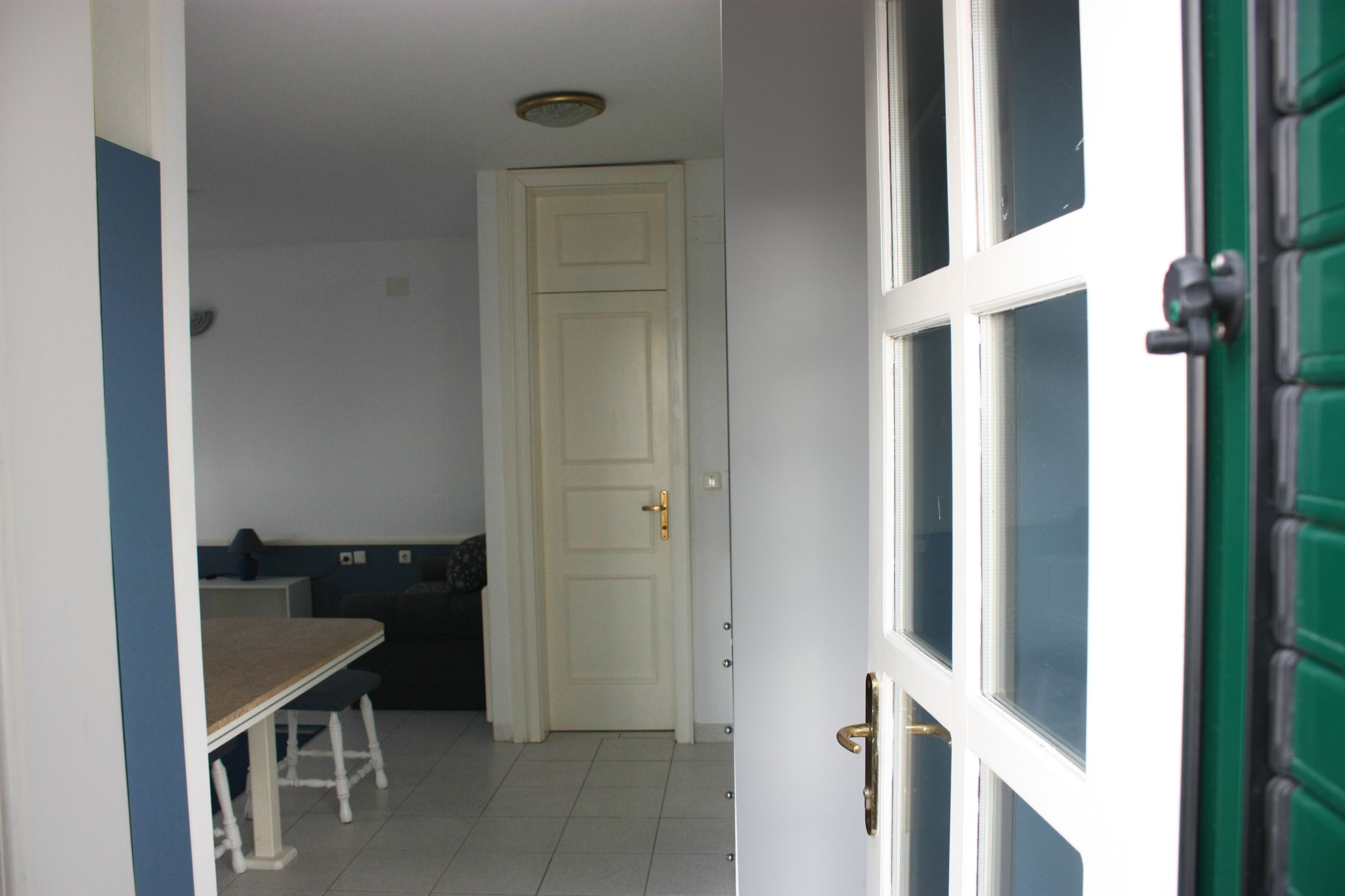 Un couloir étroit avec une porte blanche, une petite table avec un banc et une porte verte sur la droite.
