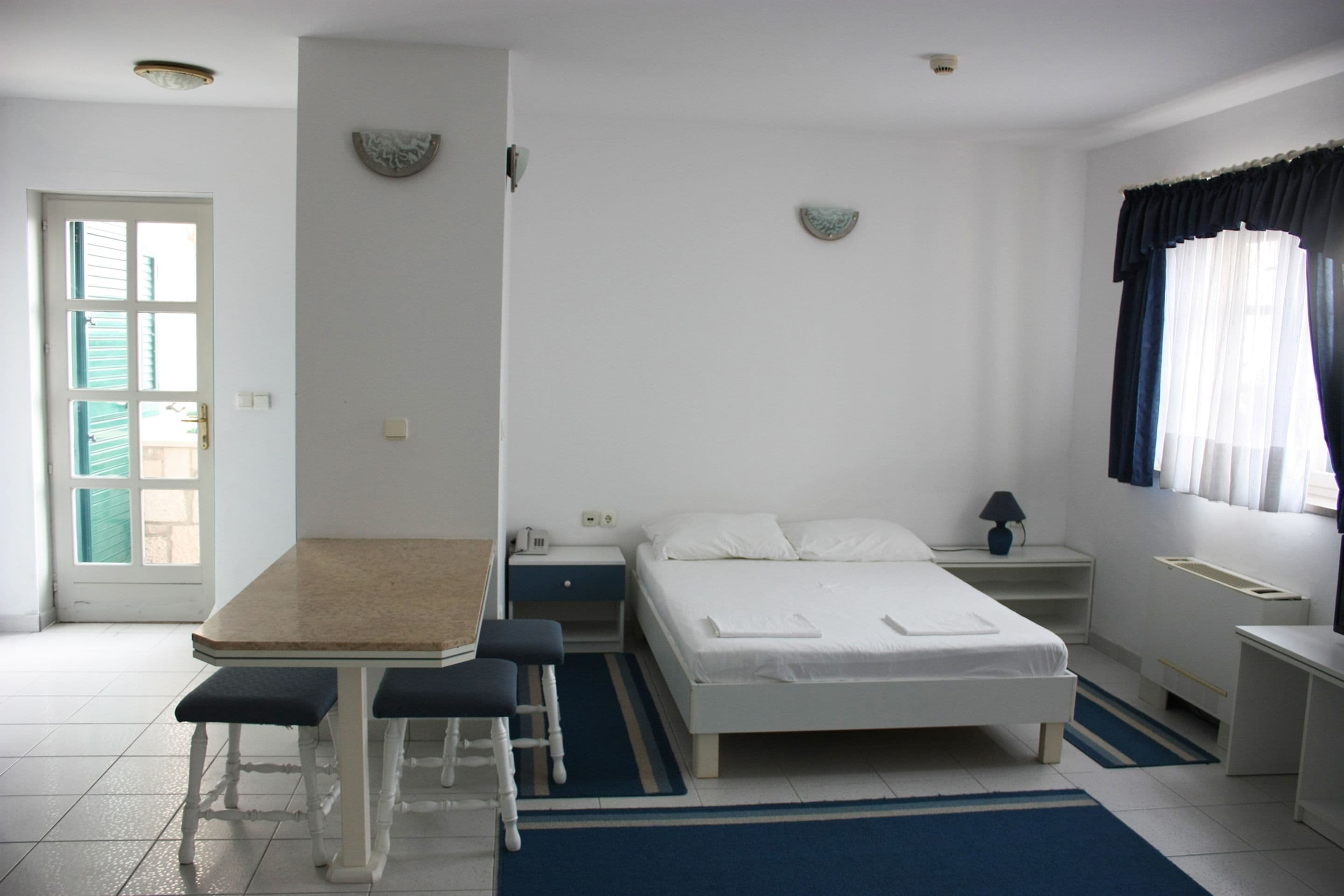 Een slaapkamer met een bed, nachtkastje, lamp en een raam met gordijnen.