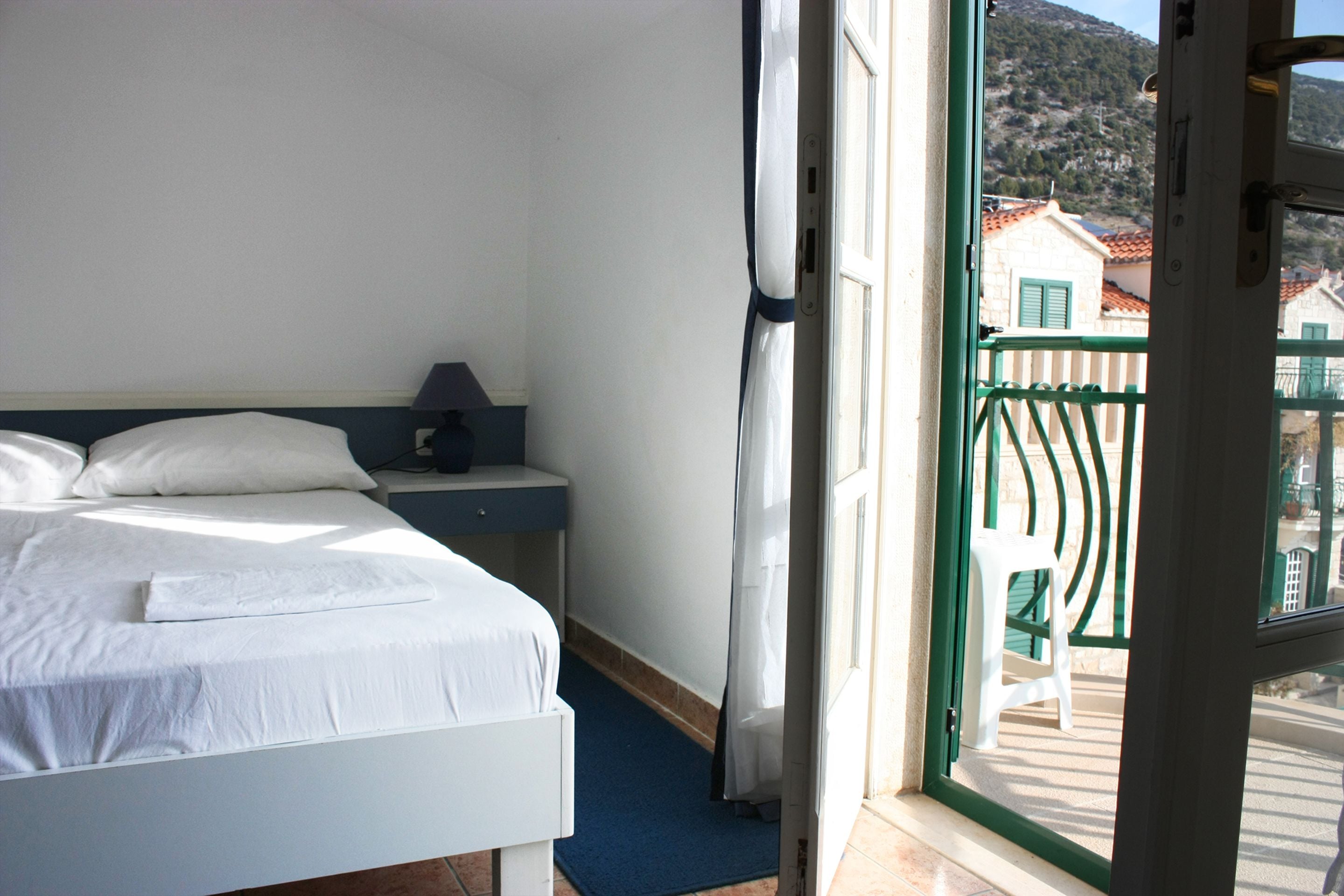 A hotel room with a bed, a nightstand, a window with a view of buildings and a balcony.