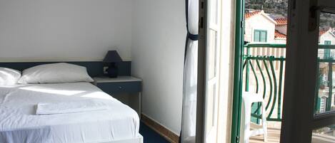 A hotel room with a bed, a nightstand, a window with a view of buildings and a balcony.