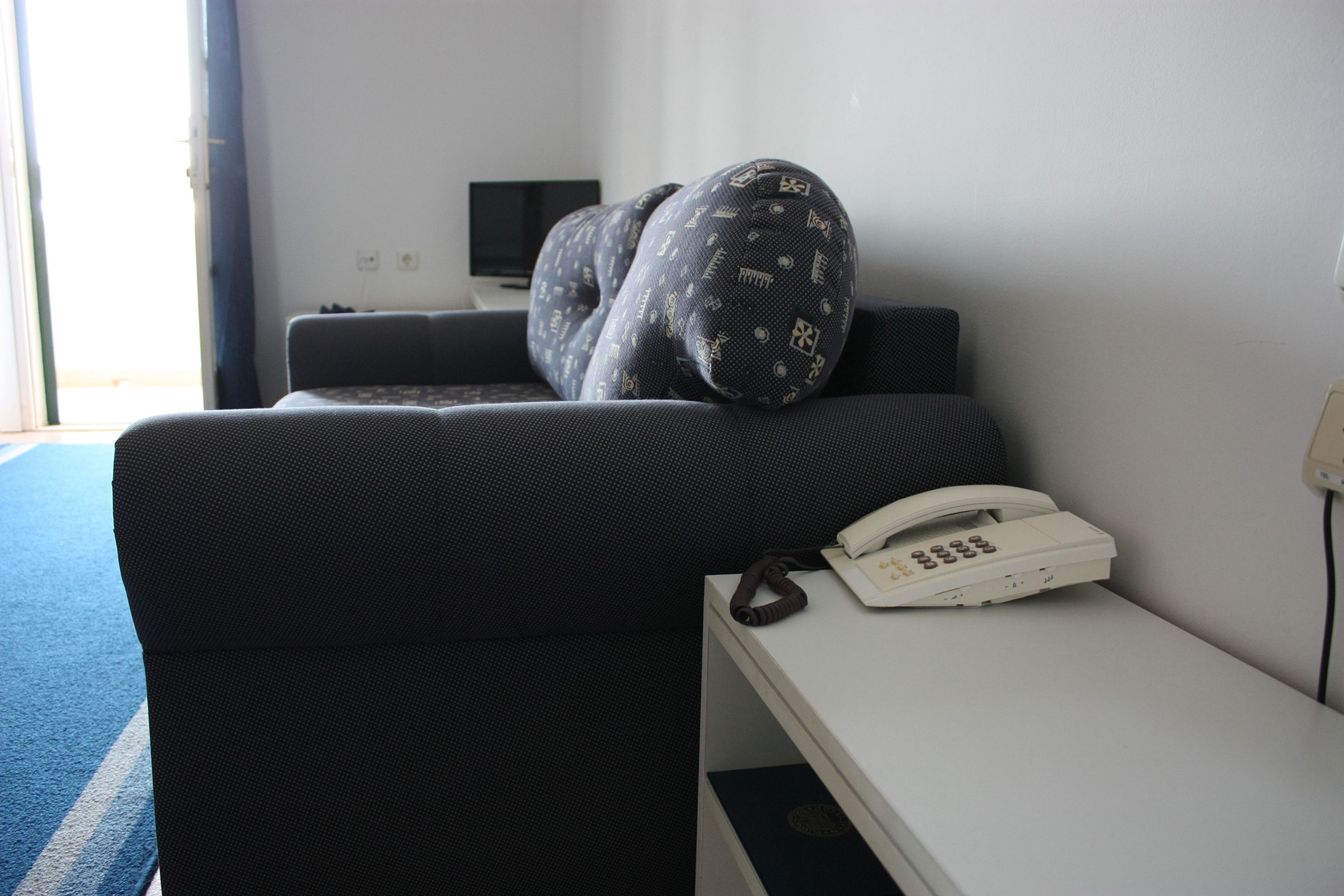 A hotel room with a bed, a bedside table with a telephone, and a television on the wall.