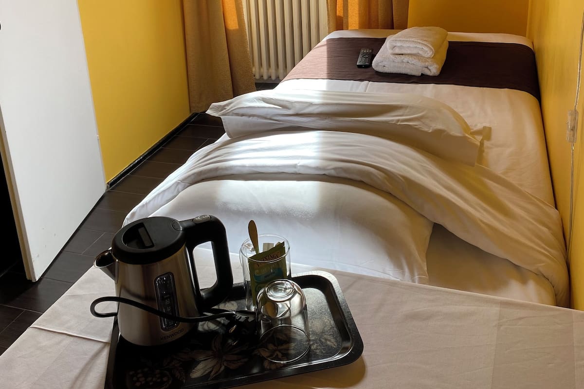 Habitación de hotel con dos camas, una ventana con cortinas, un televisor de pared y una bandeja con hervidor y vasos.
