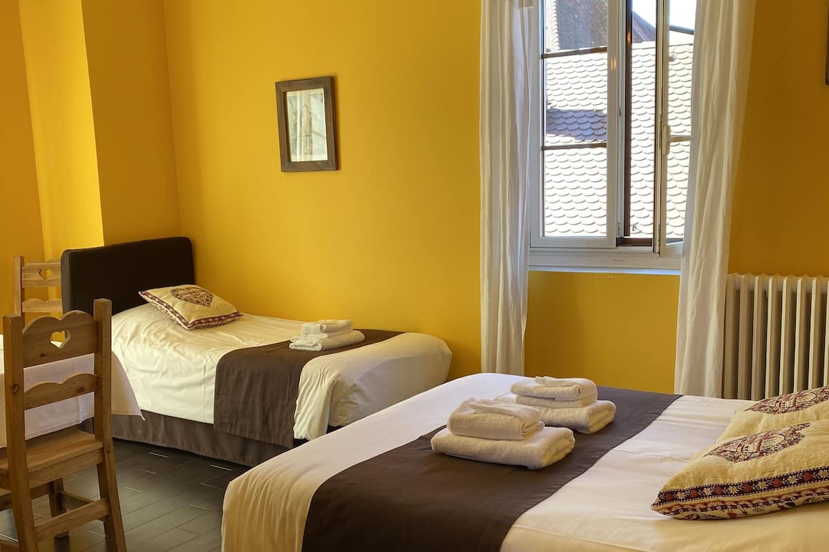 Habitación de hotel con dos camas, una silla de madera, una ventana con cortinas y un radiador.