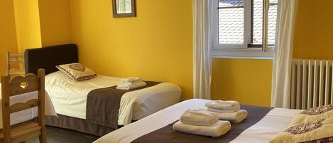 A hotel room with two beds, a wooden chair, a window with curtains, and a radiator.
