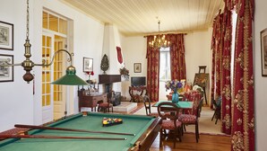 A room with a pool table, wooden flooring, a chandelier, and red curtains. - Casa d'Óbidos (Obidos)