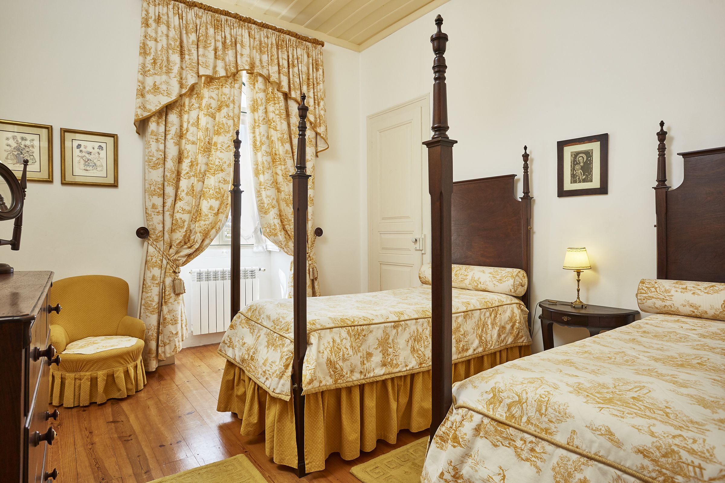 A four-poster bed with a canopy, a wooden chair, and a small table with a lamp.