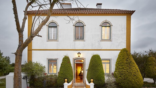 A two-story building with a yellow and white facade, a central entrance with a light fixture, and three arched windows. - Casa d'Óbidos (Obidos)