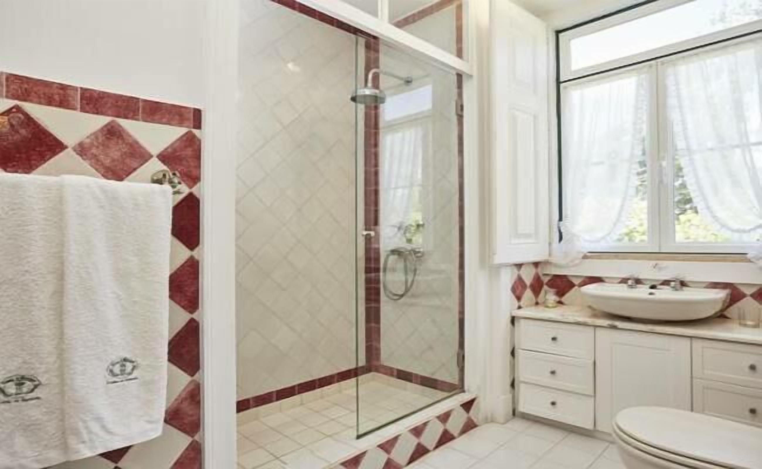 A bathroom with a glass-enclosed shower, a white sink, and a window with curtains.