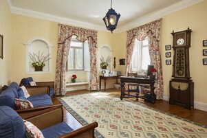 Quarto com sofá azul, escrivaninha de madeira, tapete estampado e um relógio de parede grande.