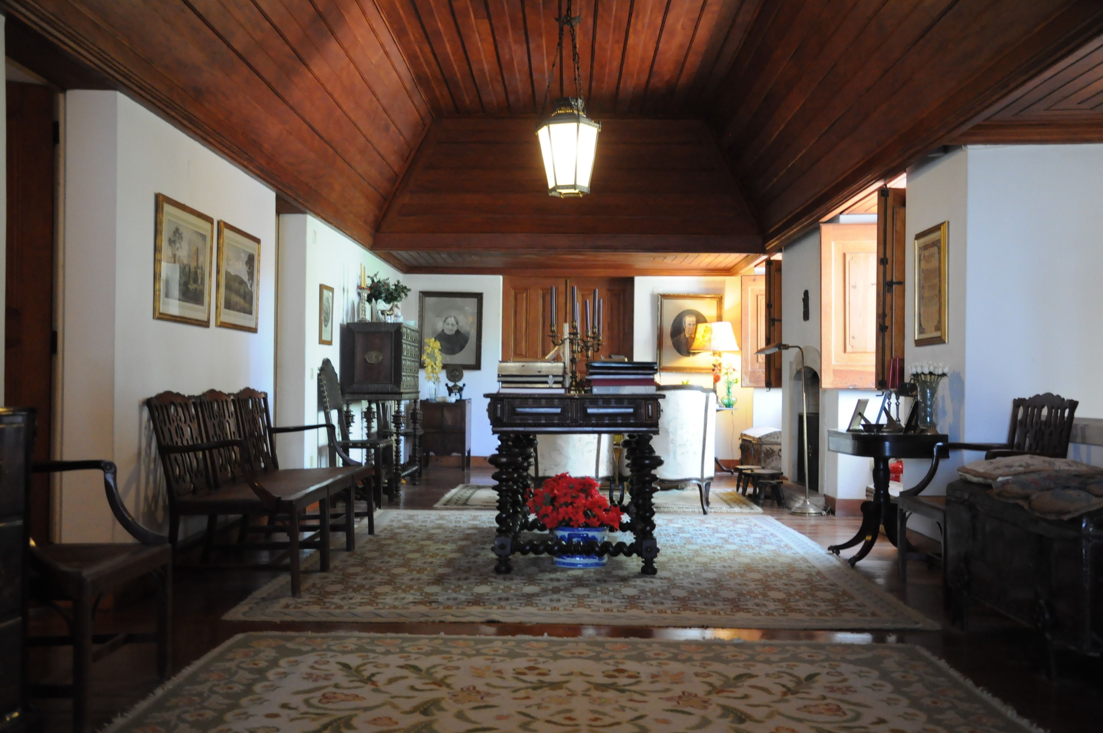 A traditional room with wooden ceilings, a central table with red flowers, and framed pictures on the walls.