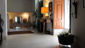 A spacious foyer with a stone bench, a standing lamp, potted plants, and a wooden door. - Quinta da Alcaidaria Mór (Ourem)