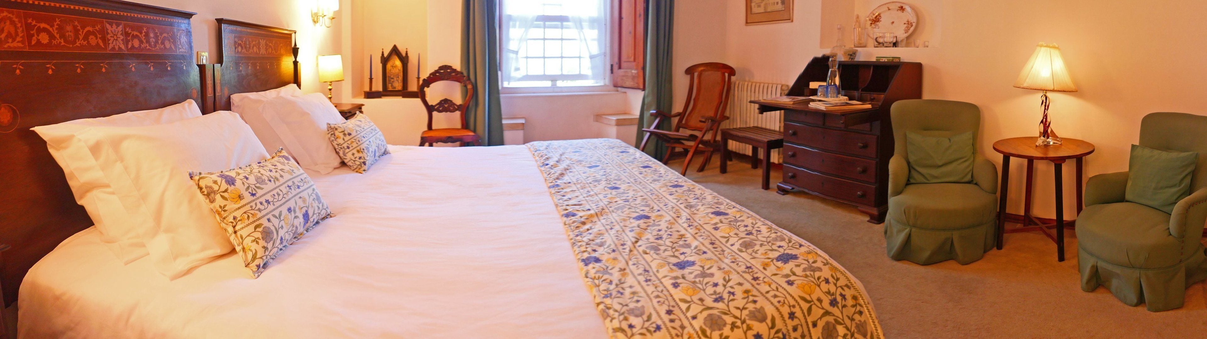 A neatly arranged hotel room with a large bed, a desk, two chairs, and a small table with a lamp.