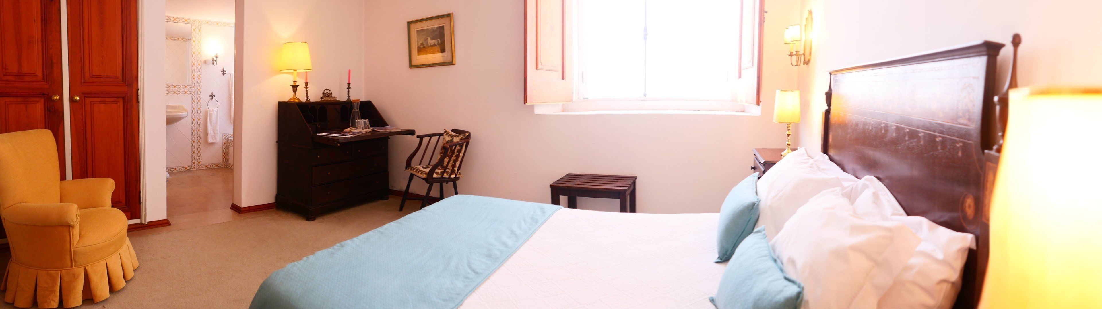 Una habitación de hotel con cama, una silla, escritorio, una mesita y ventana.