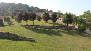A grassy area with stone walls and trees, a stone pathway, and buildings with red roofs in the background.