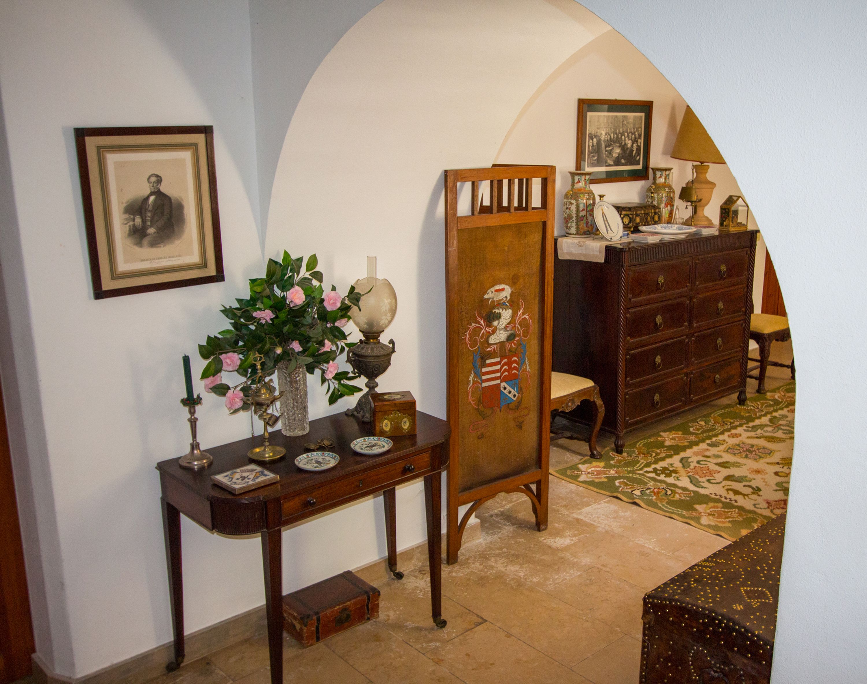A room with a wooden desk, a vase with flowers, a framed picture, and a dresser with a mirror.