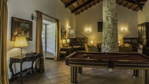 A pool table in a room with a stone pillar, a bookshelf, and a sofa. - Quinta da Alcaidaria Mór (Ourem)