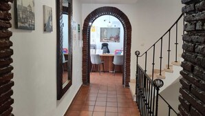 A hallway with a brick wall, a tiled floor, and a staircase with a metal railing. - Orfebre Góngora (Córdoba)