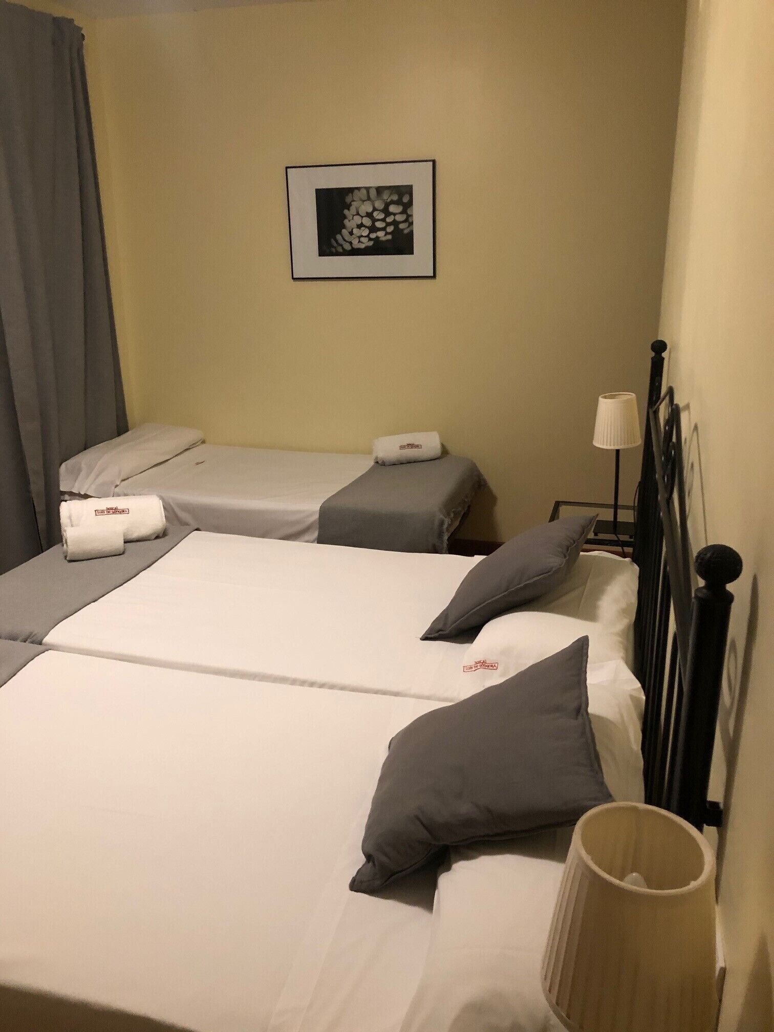 Habitación de hotel con dos camas, una mesita de noche, una lámpara y un cuadro en la pared.