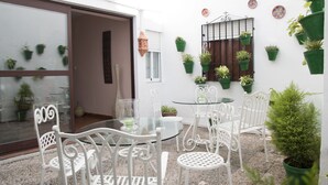 A patio with white metal chairs and a glass table, surrounded by potted plants and a decorative metal gate. - Orfebre Góngora (Córdoba)