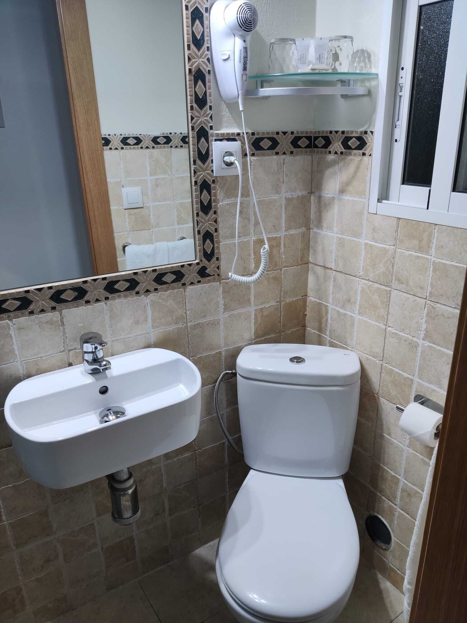 Un baño con lavamanos blanco, inodoro y un secador de pelo fijado a la pared.