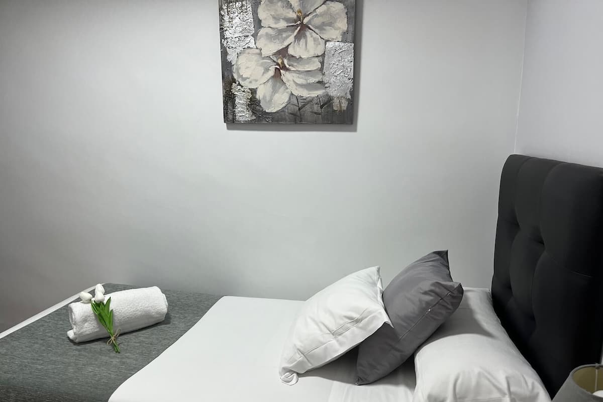 Un dormitorio moderno con una cama bien hecha, un cabecero gris y una obra de arte floral en la pared.