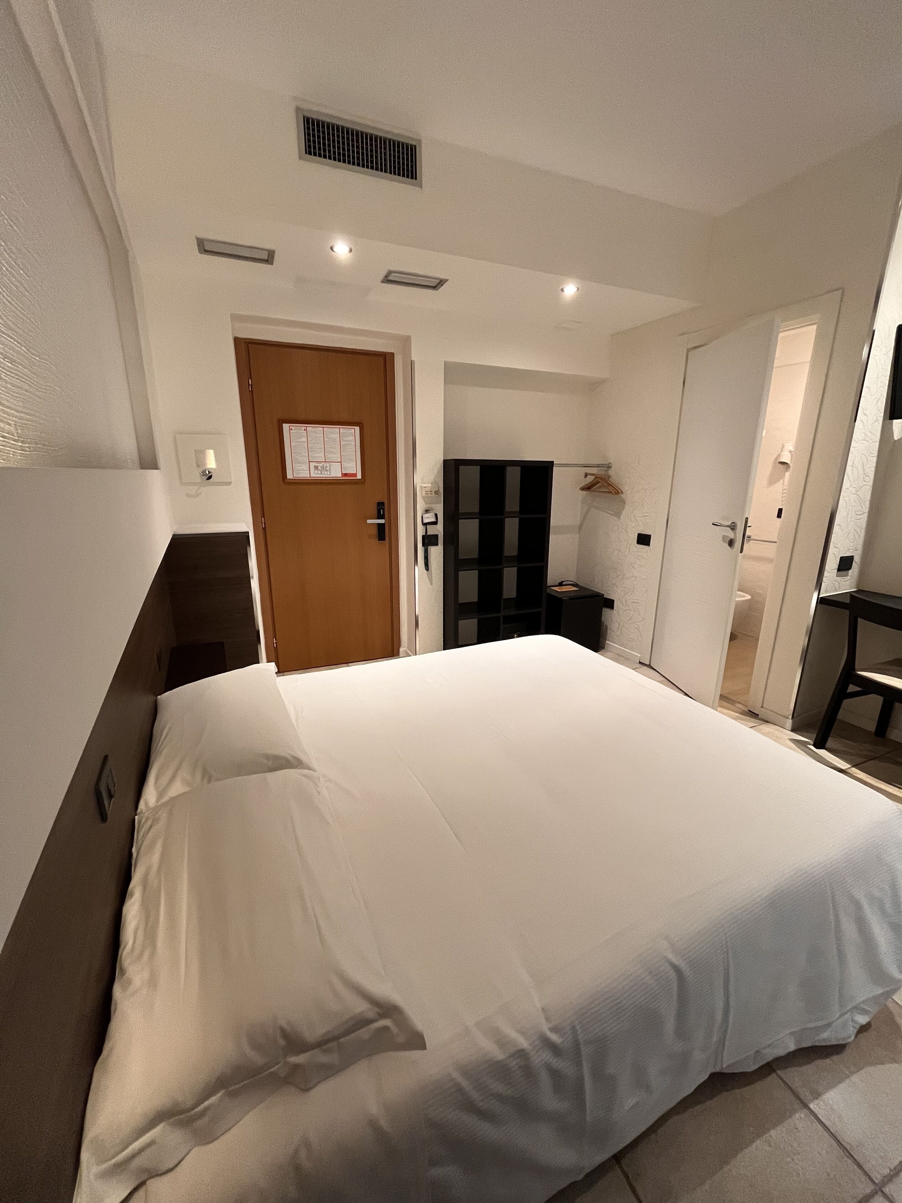 Une chambre d’hôtel avec un grand lit, une armoire, un bureau et une salle de bain visible à travers une porte ouverte.
