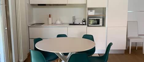 Una cocina moderna con armarios blancos, un microondas y un comedor con una mesa redonda y sillas color turquesa.