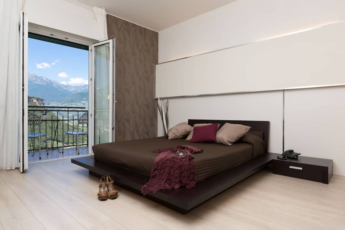 A modern bedroom with a large bed, a bedside table, and a view of mountains through a balcony.
