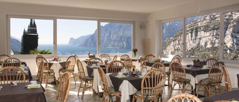 A restaurant with multiple tables and chairs, large windows with a view of cliffs and the sea.
