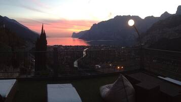 Un balcon offrant une vue sur un coucher de soleil se reflétant sur une étendue d’eau, le tout étant entouré de montagnes.