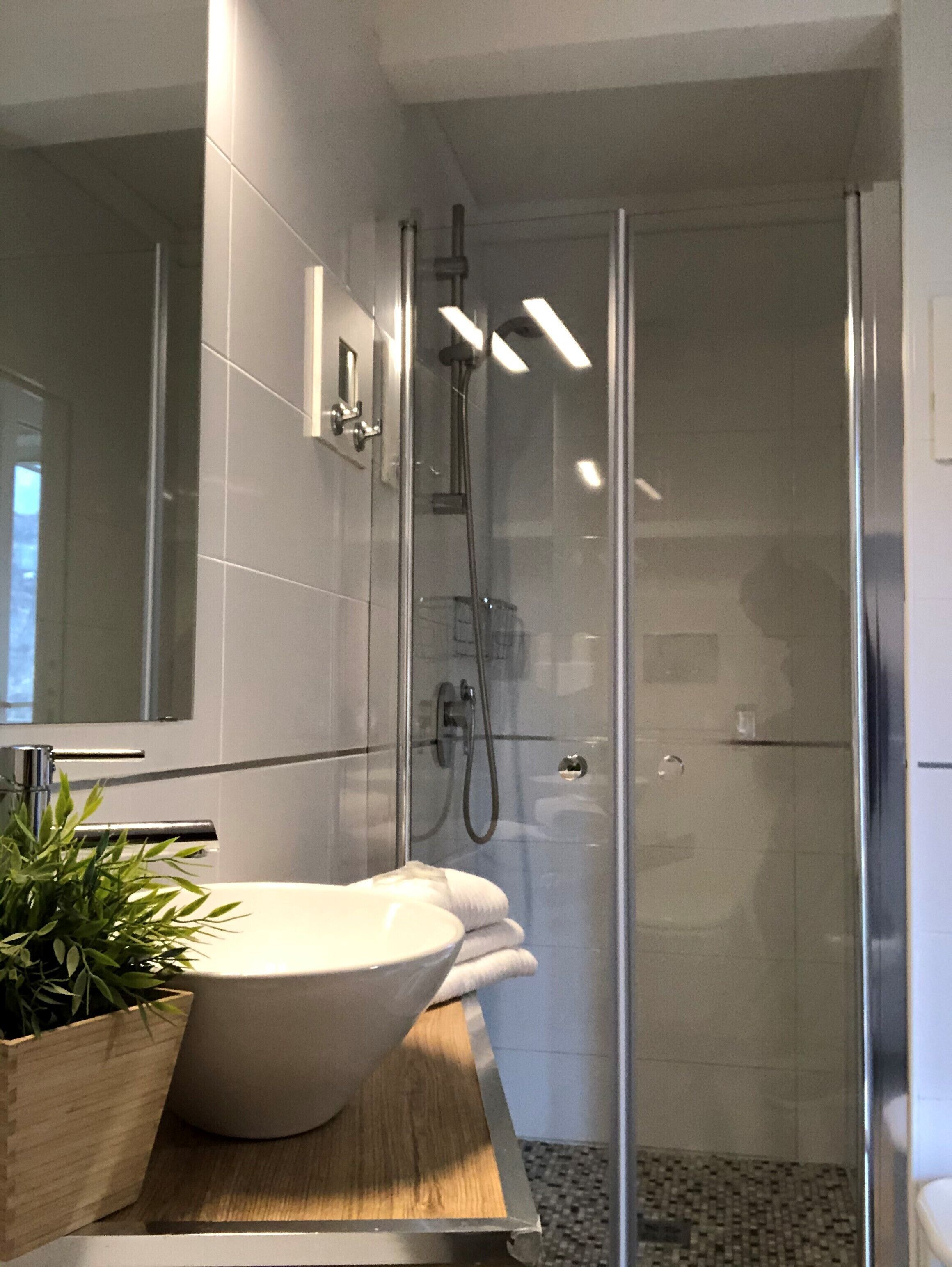 Une salle de bain moderne avec un grand lavabo blanc, une douche en verre et un plan de toilette en bois.