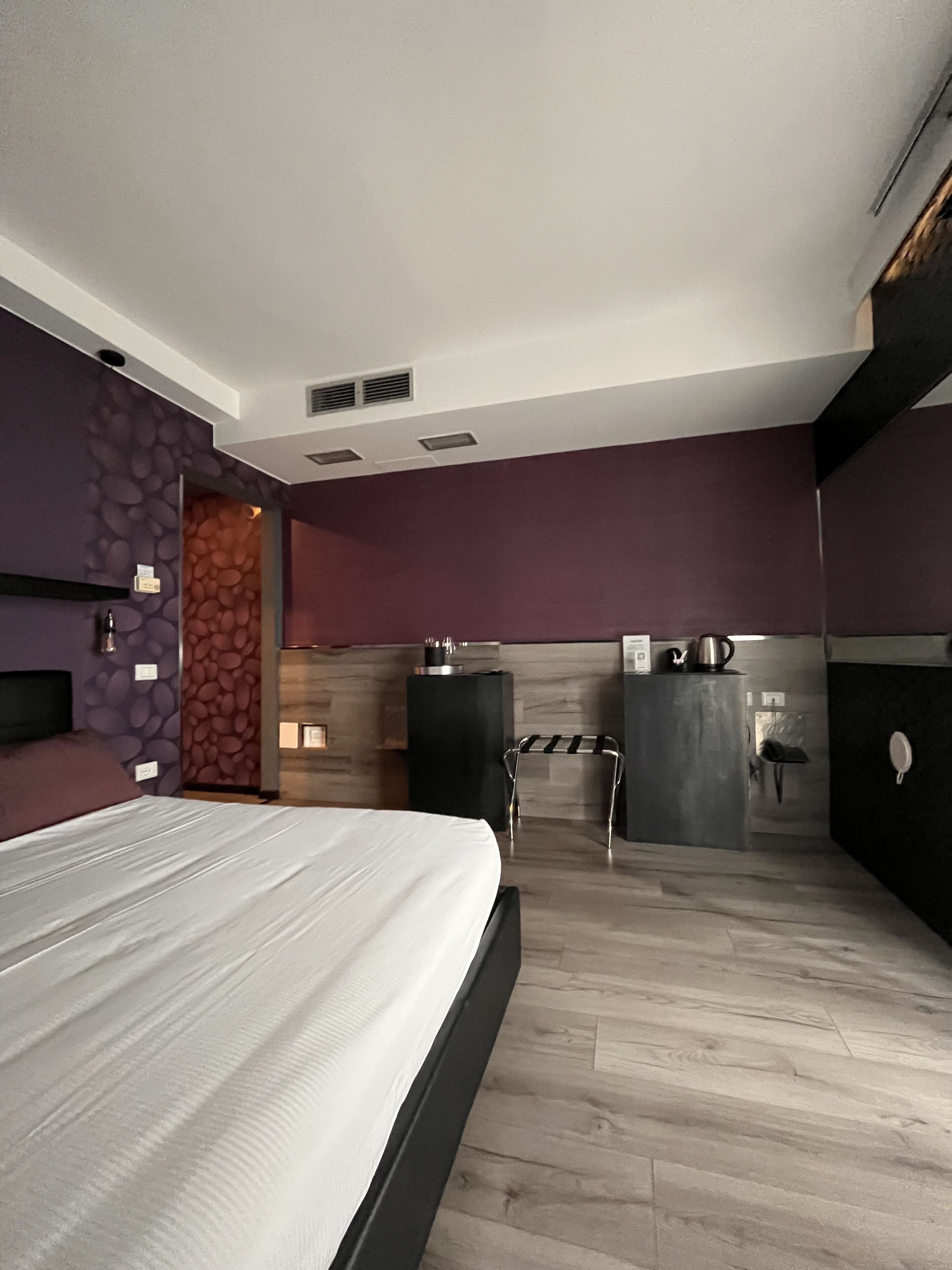 A modern hotel room with a large bed, a small kitchenette, and a bathroom.