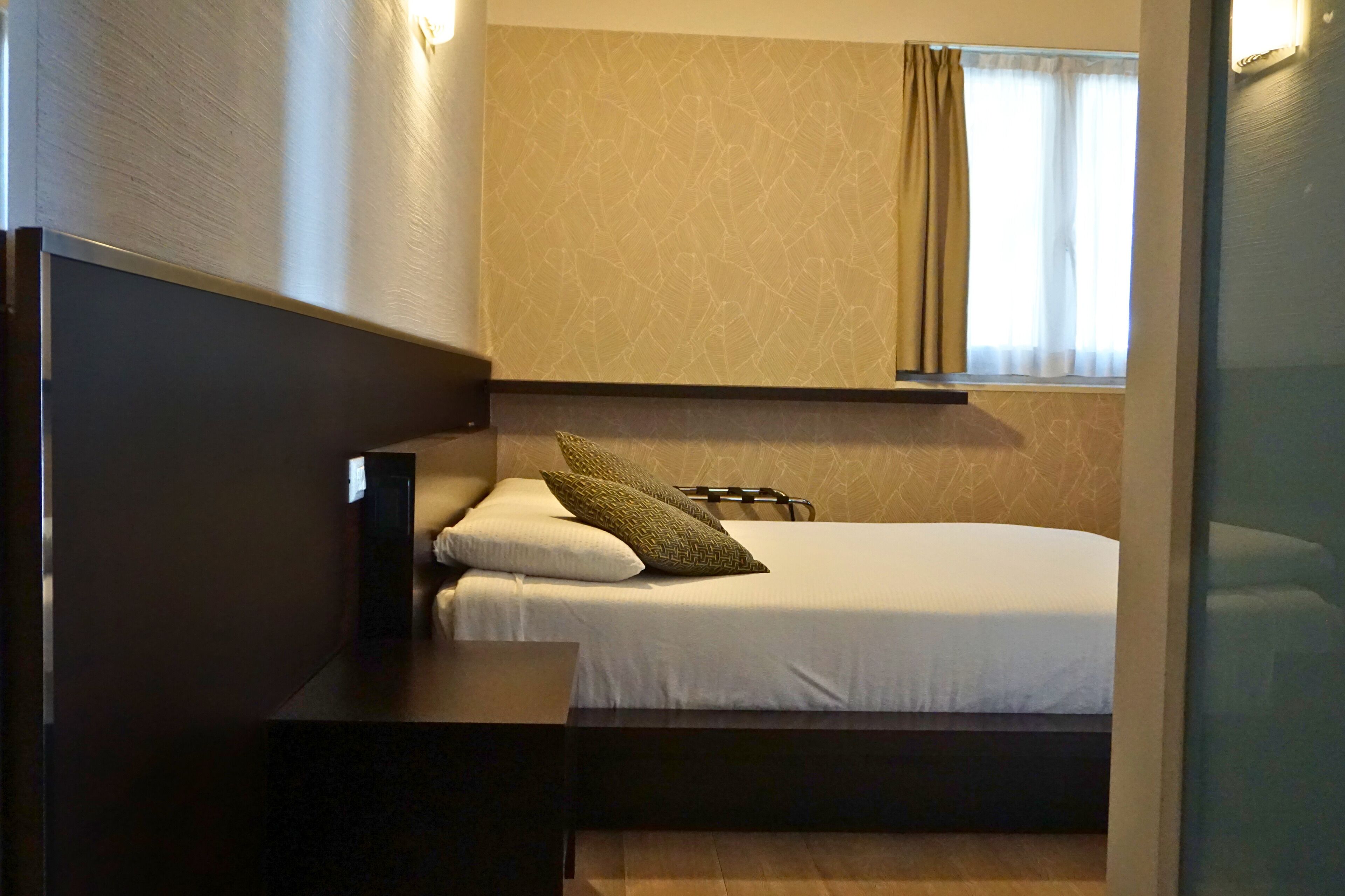 A hotel room with a bed, bedside table, and a window with curtains.