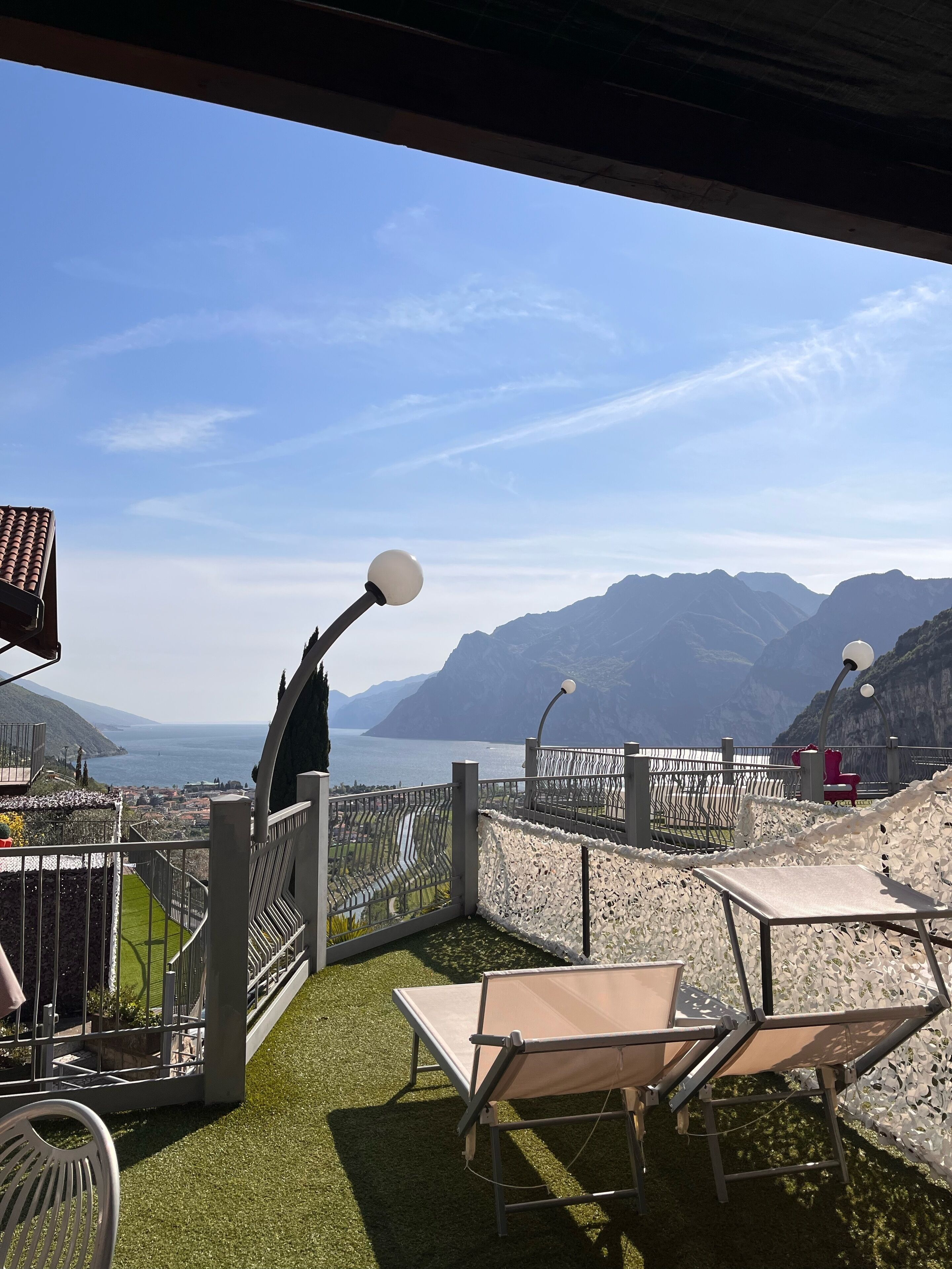A terrace with a view of the sea and mountains, featuring a table and chairs, and a decorative fence.
