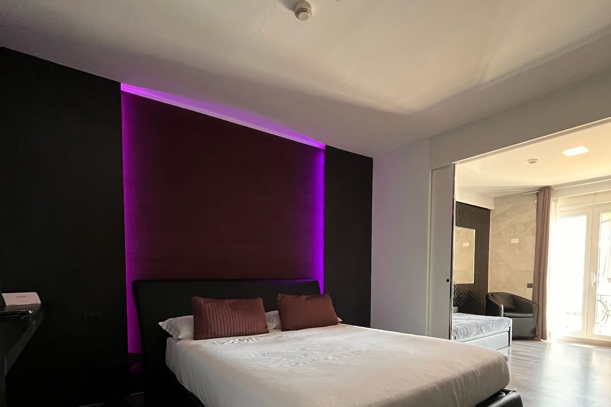 A modern bedroom with a large bed, dark walls, and a purple accent wall.