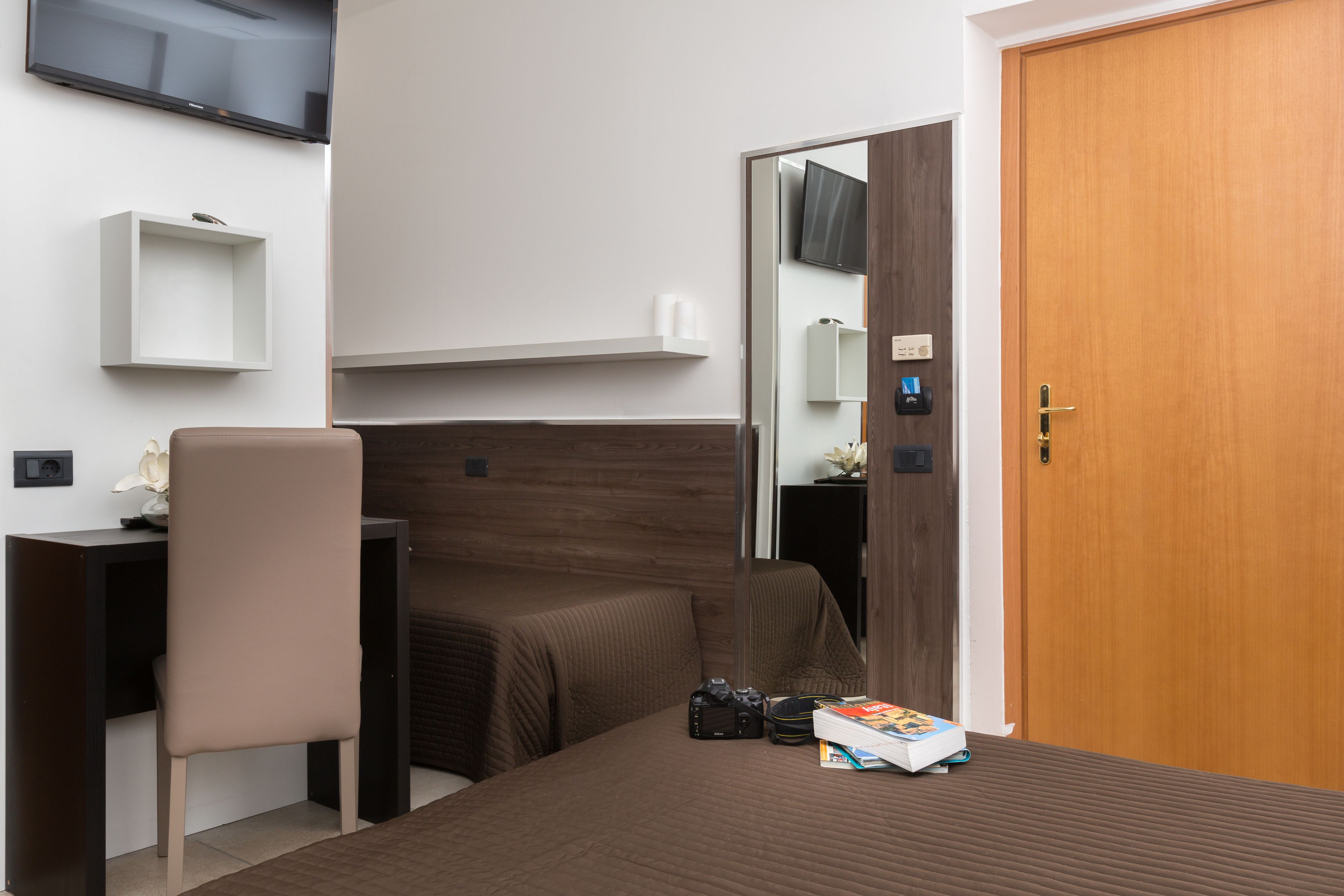 Habitación de hotel con cama, escritorio, silla, televisión y puerta de madera.