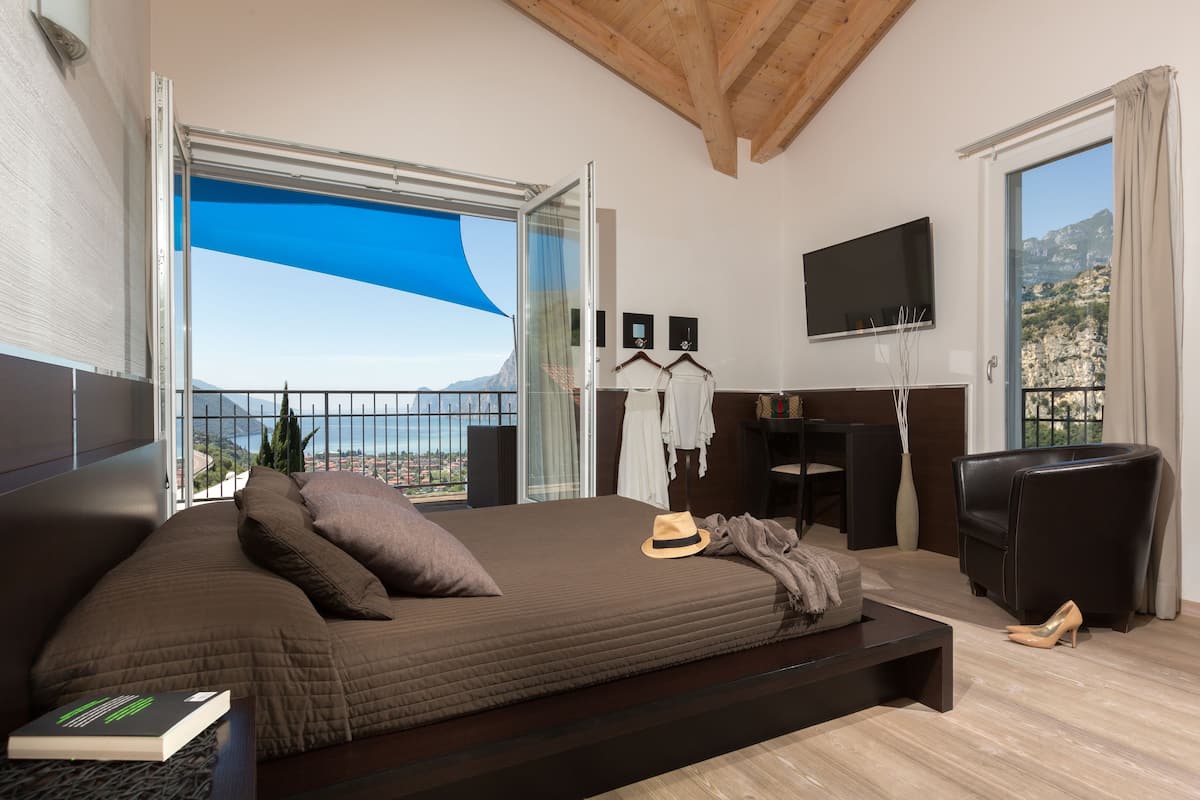 A modern bedroom with a large bed, a TV, and a balcony with a view of the mountains.