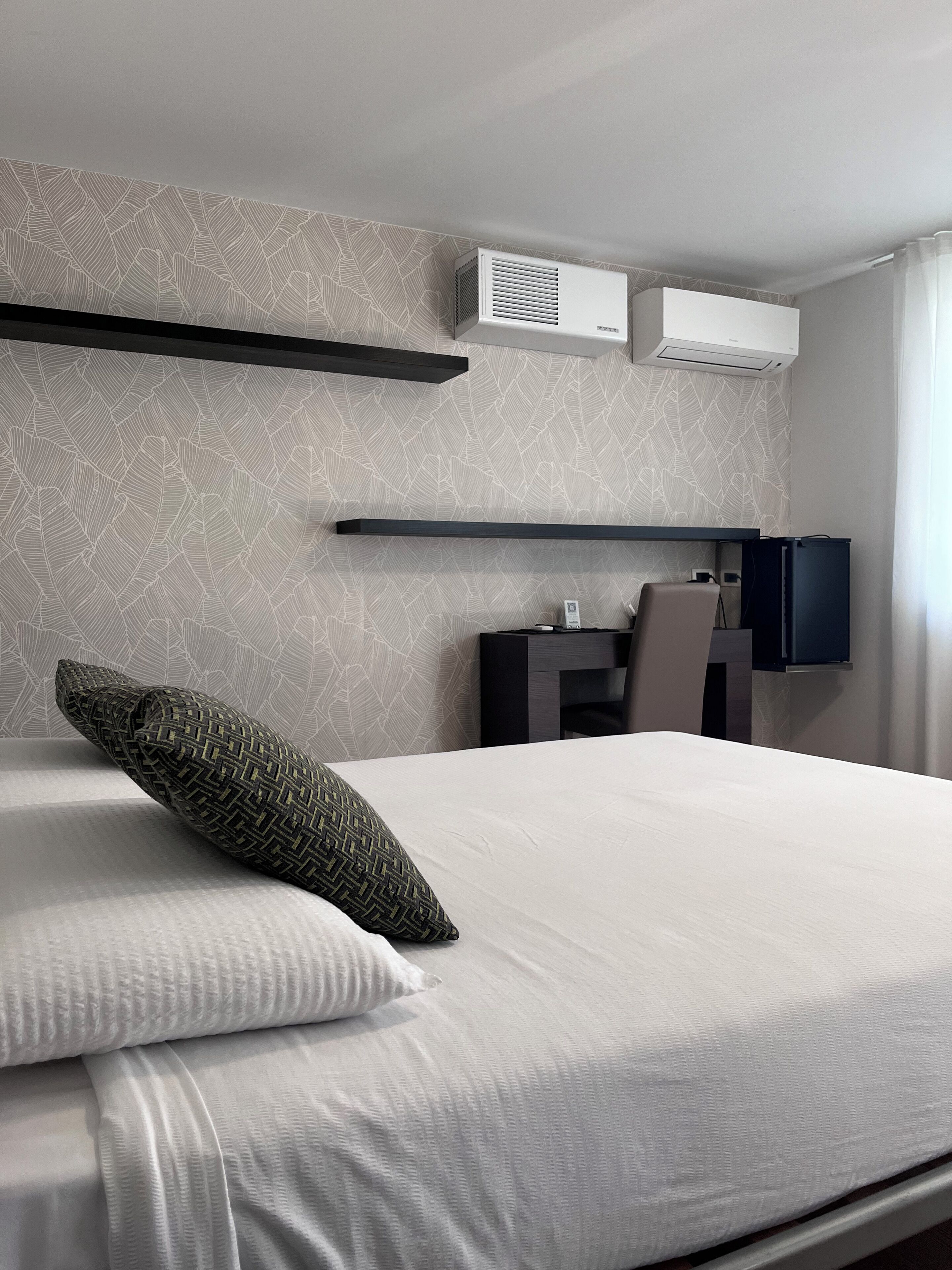 Ein Hotelzimmer mit einem Bett, einem Schreibtisch, einem Sessel, einem Flachbildfernseher und einer Klimaanlage.