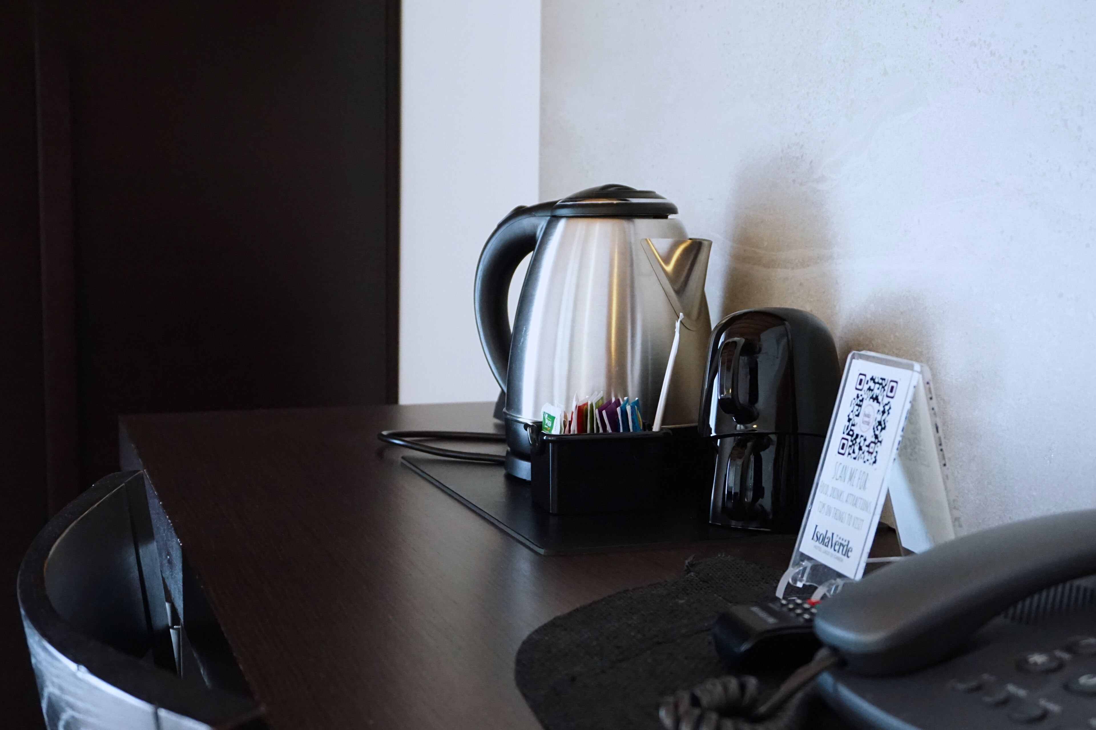 Habitación de hotel con cafetera, teléfono y un cartel con un código QR.