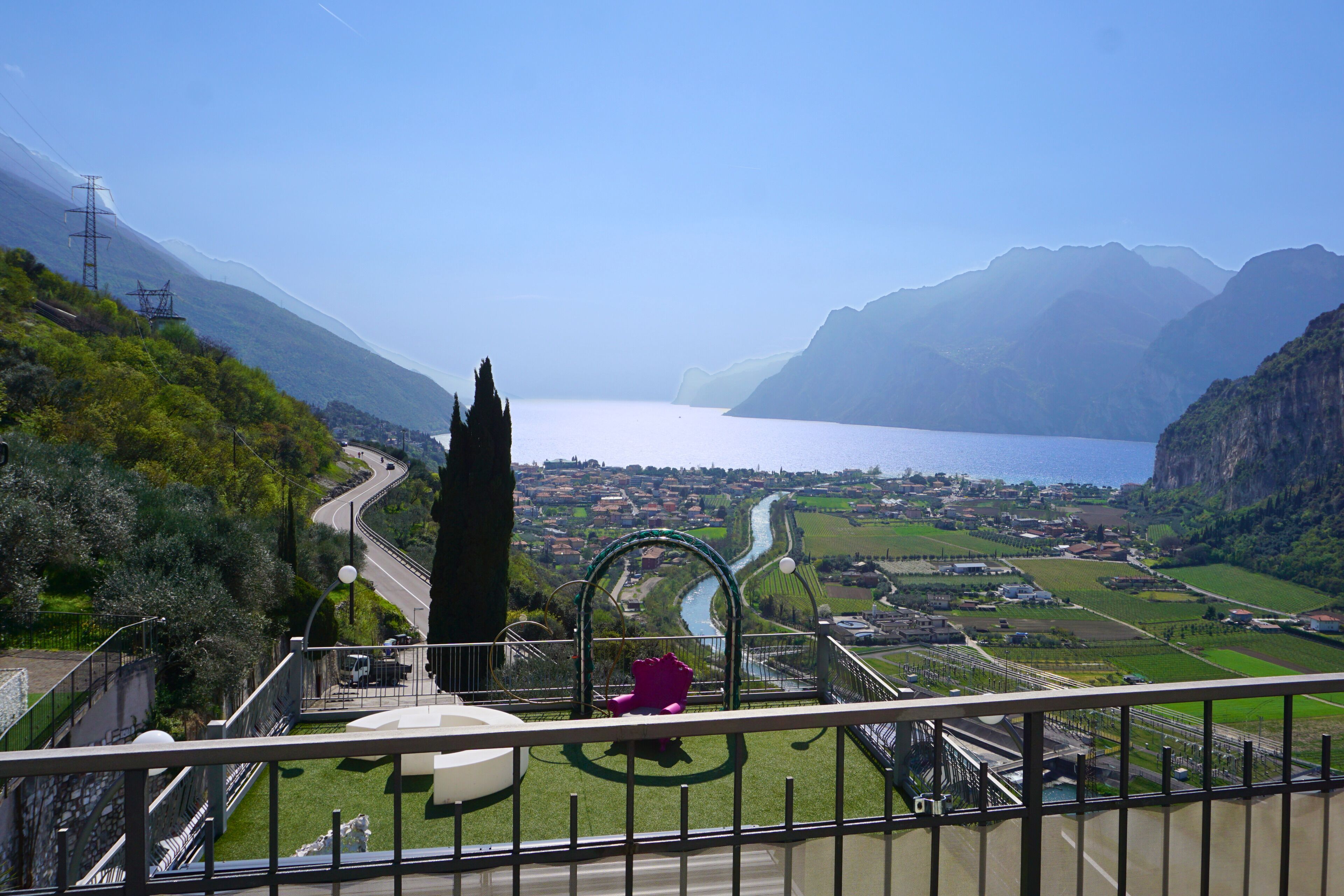 A scenic view from a balcony overlooking a valley with a river, mountains, and a distant town.